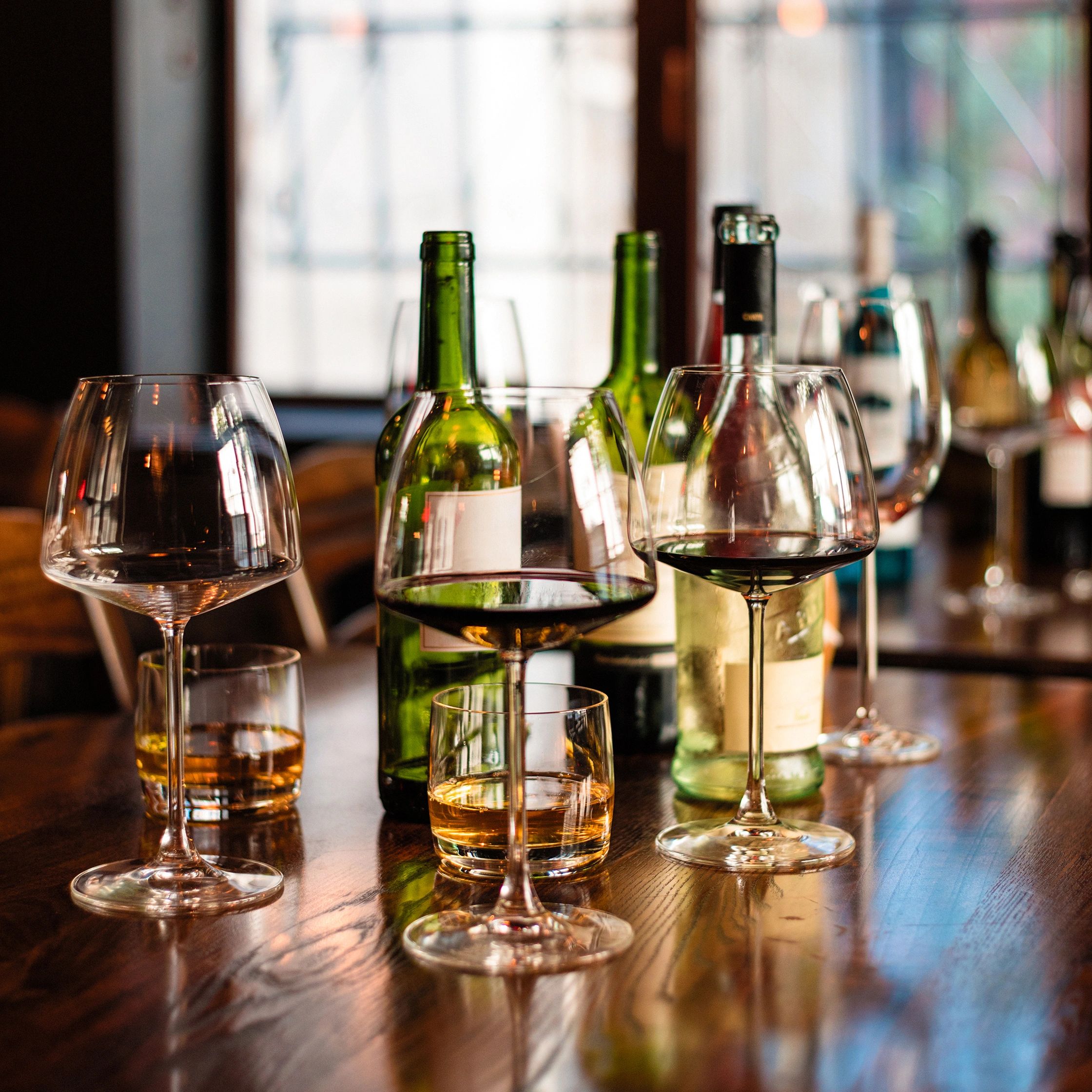 Wine glasses and bottles on a polished wooden table in a cozy setting.