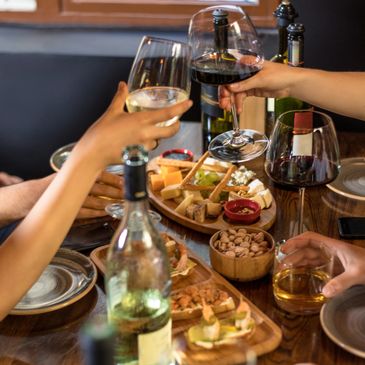 People clinking glasses over a table with wine and appetizers.