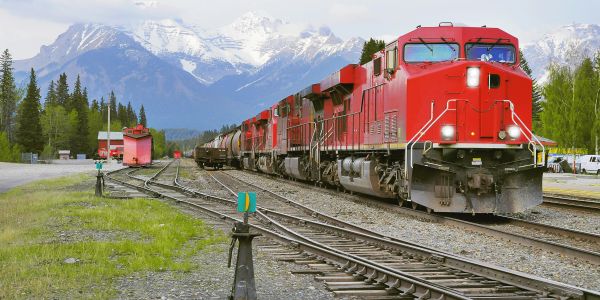 Red train moving on tracks with mountains in background.