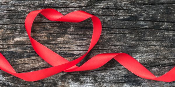 Red ribbon shaped as a heart on wooden surface.