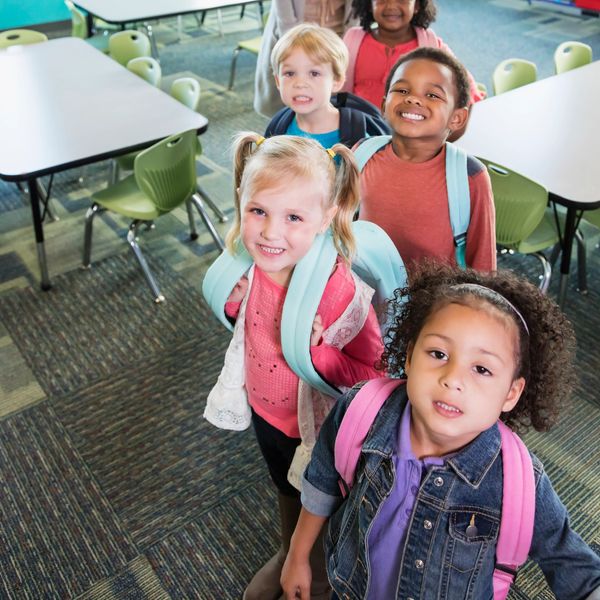 A group of smiling elementary school children with backpacks in a classroom.