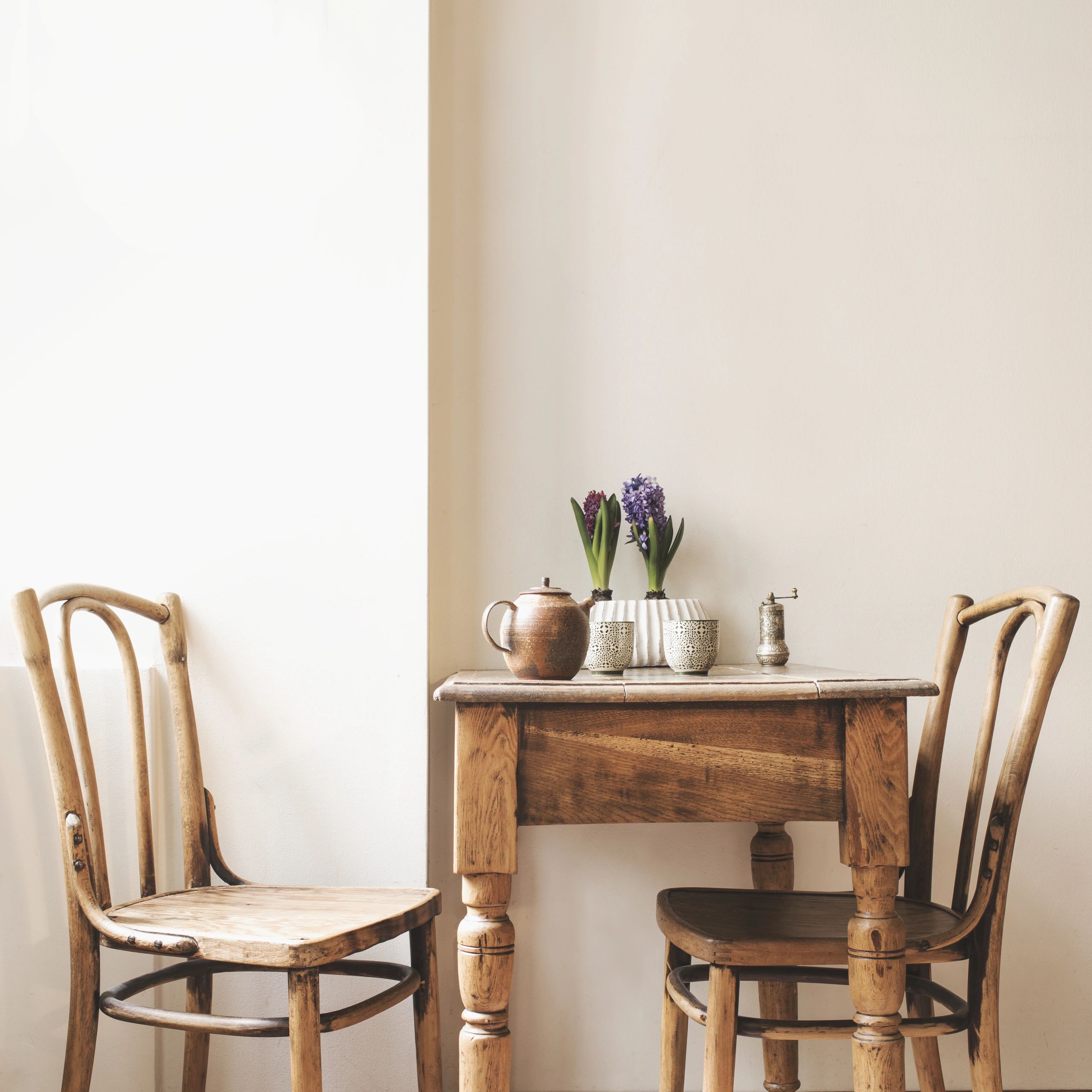 Rustic wooden table with two chairs and flower pots in a cozy corner.