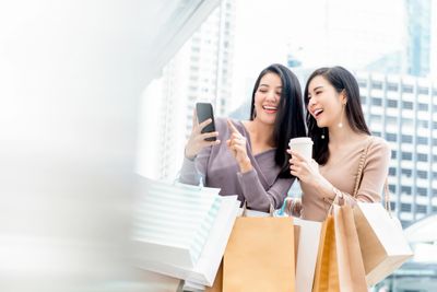 Two women happily shopping and looking at a phone together.