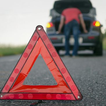Warning triangle on road by broken-down car.