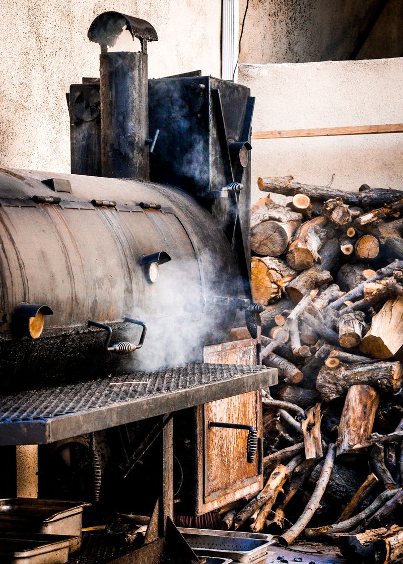Old smoker grill in use with adjacent woodpile