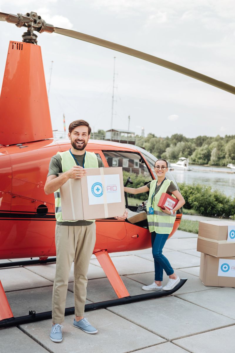 Help people. Joyful two volunteers packing cases and standing near helicopter