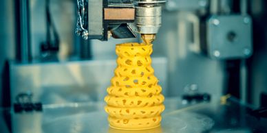 3D printer creating a yellow spiral vase with intricate patterns.