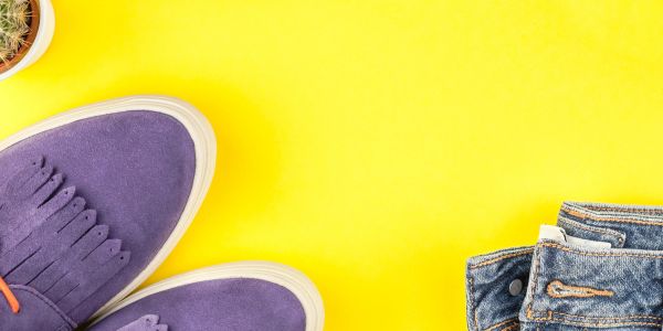 Purple shoes and folded jeans on a bright yellow background.