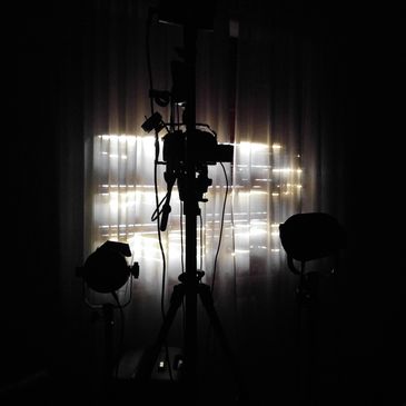 Silhouettes of lighting and camera equipment against a softly lit curtain.