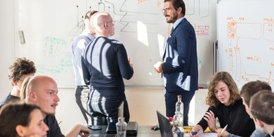 A team collaborates in a bright meeting room, discussing ideas by a whiteboard.