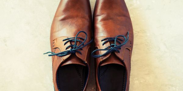 Pair of brown leather dress shoes with blue laces on a light surface.