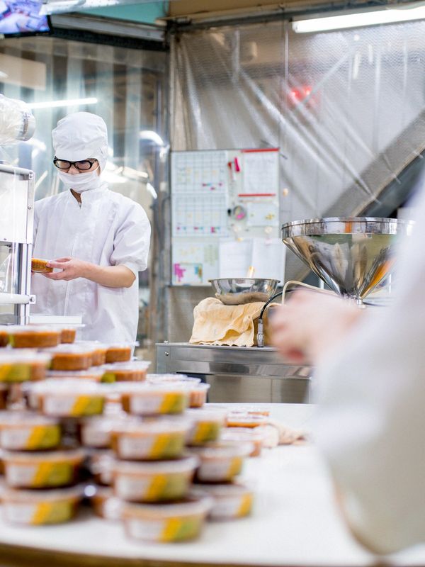 Worker in a cleanroom suit inspecting packaged food products in a factory.