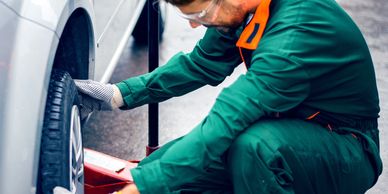 Mechanic in green coveralls changing a car tire outdoors on a rainy day.