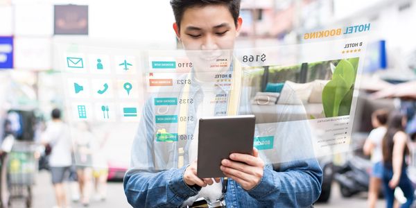 Young man using tablet for futuristic hotel booking interface on busy street.