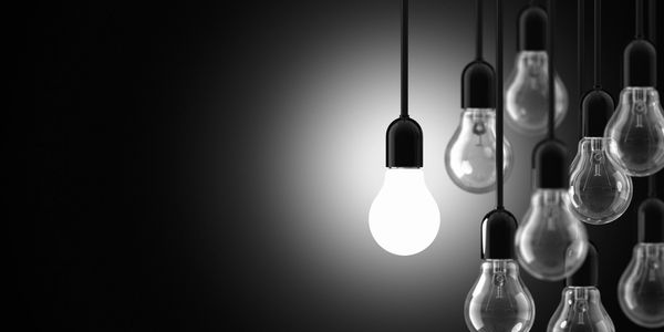 A single illuminated light bulb among many unlit bulbs.