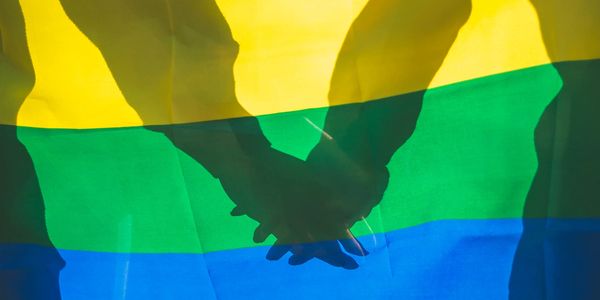 Shadows of two people holding hands behind a rainbow pride flag.