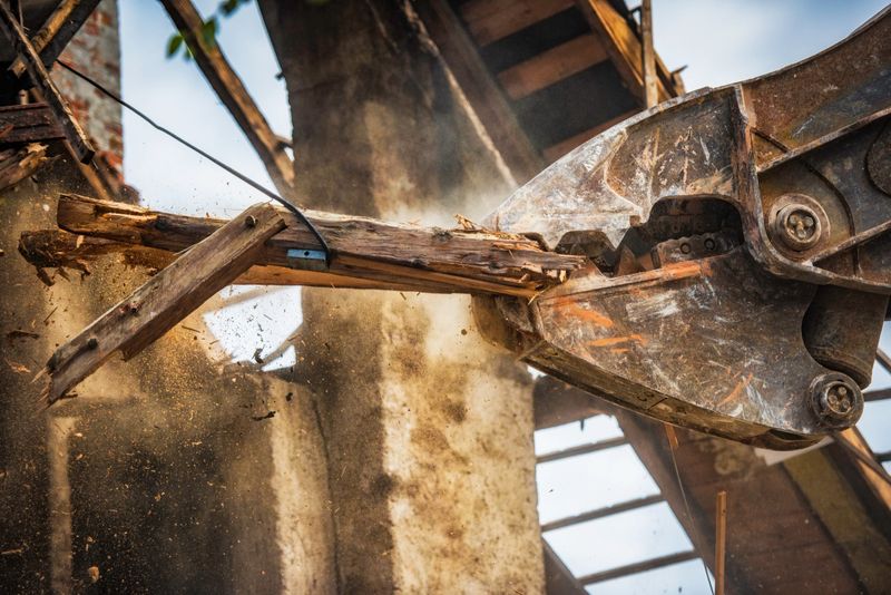 Close-up photo of an excavator arm destroying a roof of a house.