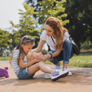 A mother helps her daughter who hurt her knee while skateboarding.