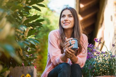 Woman enjoying a drink outdoors surrounded by plants.