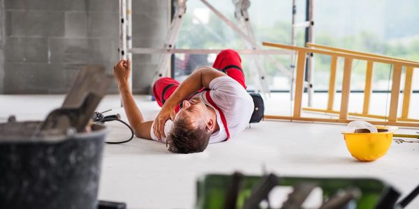 Injured construction worker lying on the floor holding his shoulder in pain.