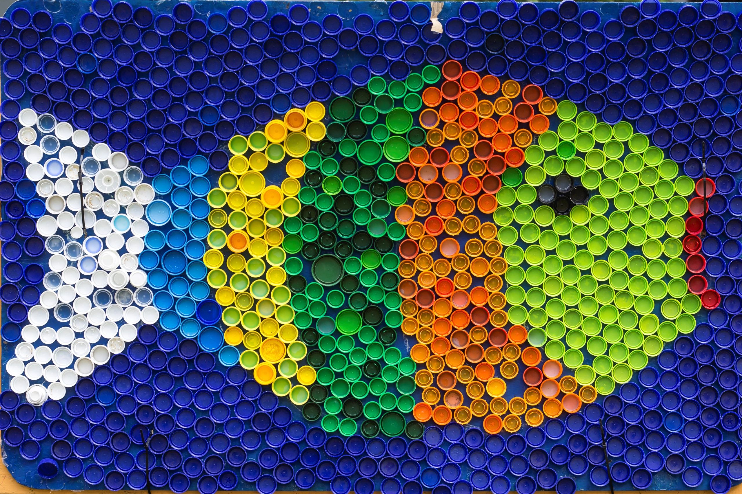 Colorful mosaic made from plastic bottle caps arranged in a flower pattern.
