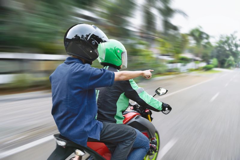 Rear view of passenger directing the way to motorcycle taxi driver on the street