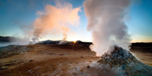 Geysers steaming in a barren landscape at sunrise.