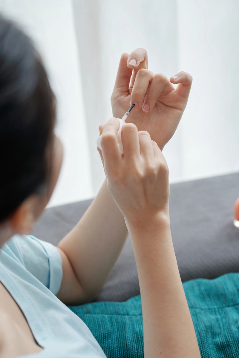 From above shot of unrecognizable woman using brush to apply nail polish on fingernails