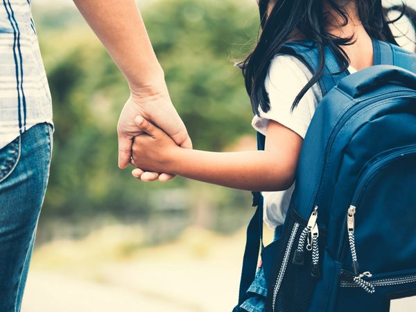 An adult holding a child's hand as they walk together outdoors.