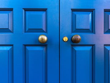 Close-up of blue double doors with round brass knobs.