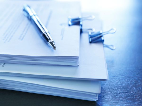Stack of legal documents with a pen on top and binder clips separating stacks of the papers.