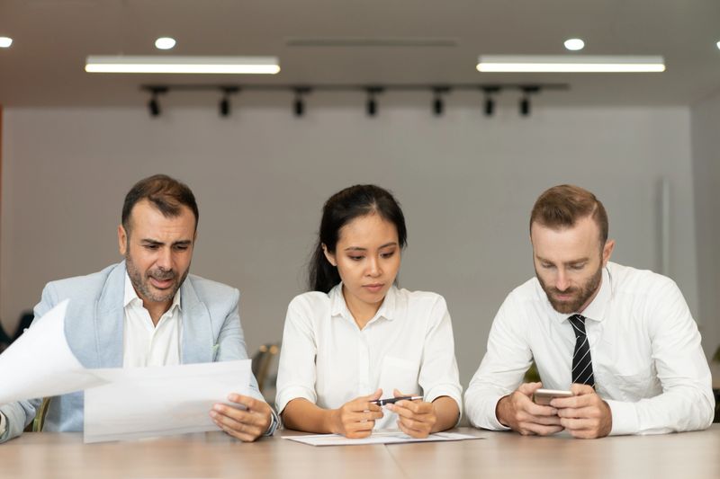 Focused business people working with documents at desk in office. Businesspeople sitting with blurred interior in background. Business team concept. Front view.