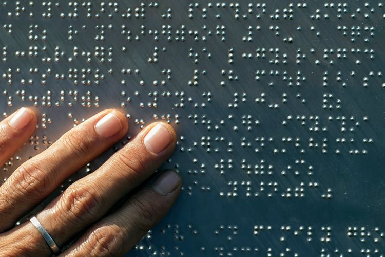 Image of left hand reading braille on black paper