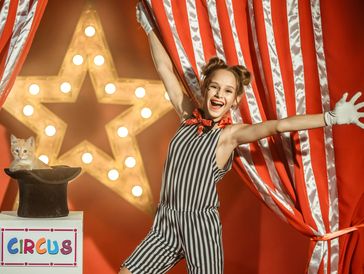 Smiling young circus performer with a kitten in a hat and bright star backdrop.