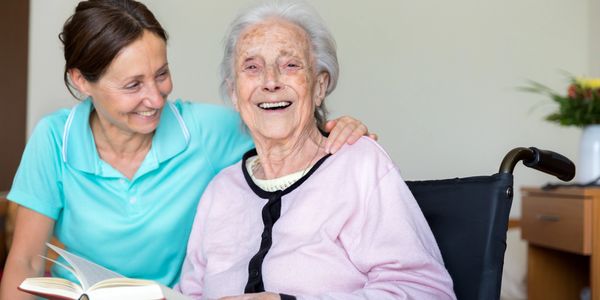 Caregiver and elderly woman sharing a joyful moment with a book.