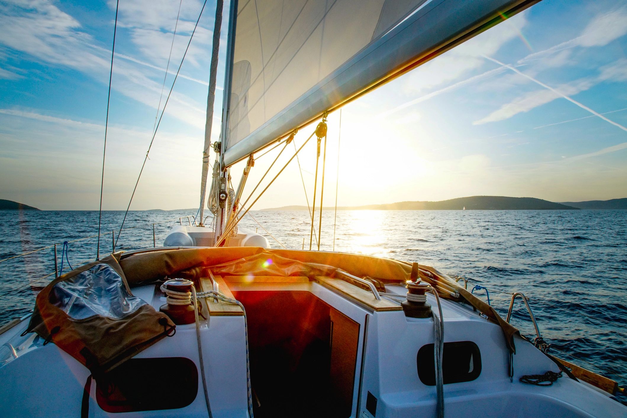 Sailing boat cruising on calm sea with sunset in the background.