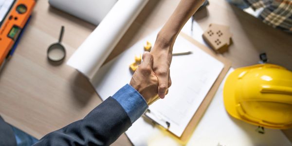 Two people shaking hands over a construction plan.