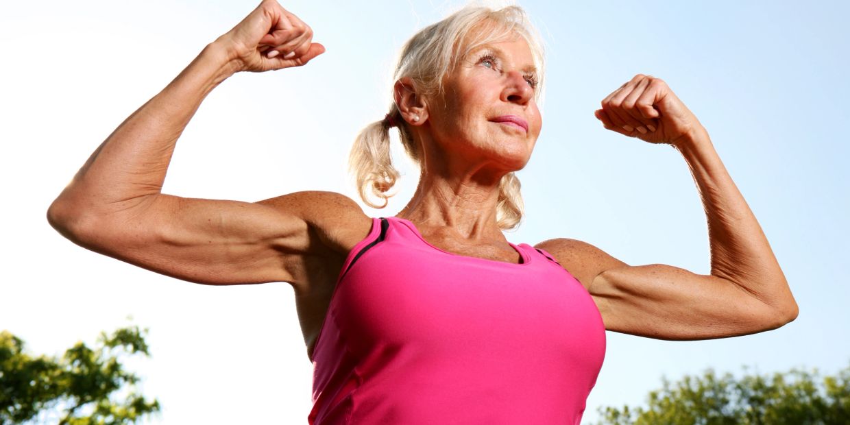 Elderly woman flexing muscles outdoors.