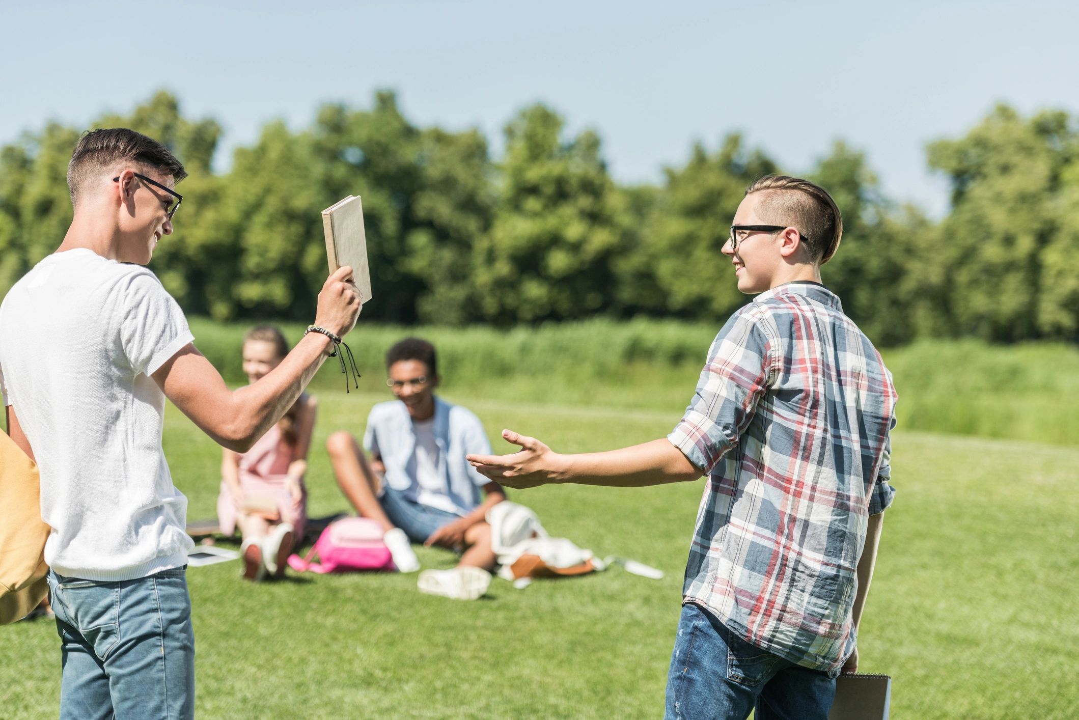 Two boys with glasses happily interacting outdoors with a group in the background.