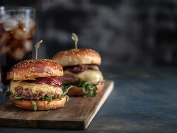 Gourmet cheeseburgers with grilled onions and arugula on sesame buns, served with soda.