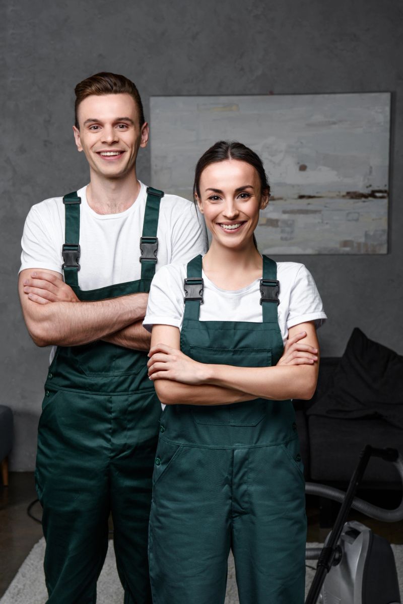 cheerful young professional cleaners standing with crossed arms and smiling at camera