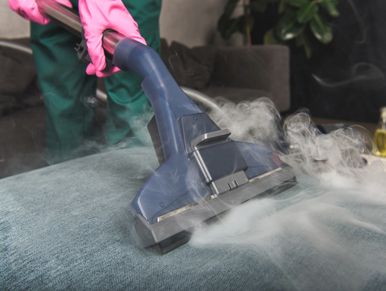 Person using a steam cleaner on upholstery with pink gloves.