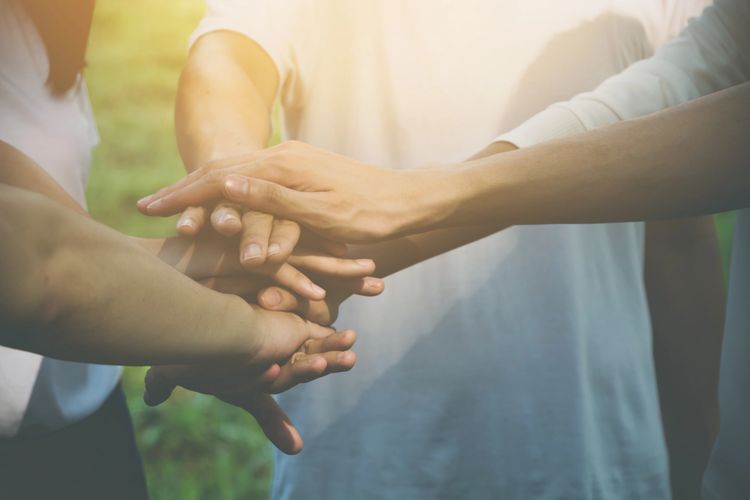 A group of people stacking hands in unity outdoors.