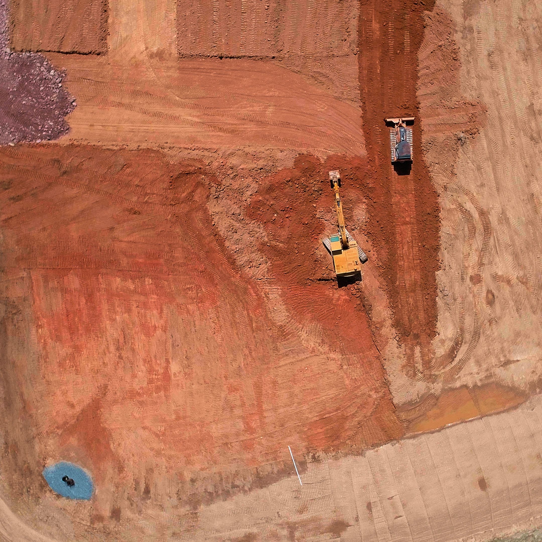 Aerial view of construction vehicles working on red soil.