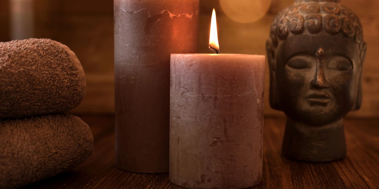 Burning candles, folded towels, and Buddha statue create a serene spa atmosphere.