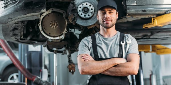 Confident mechanic standing in front of a car on a lift.