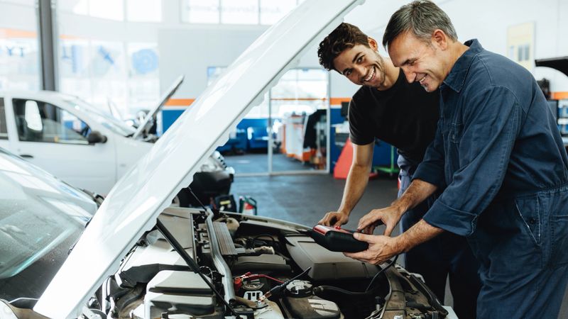 Two happy automobile mechanics doing car engine checkup with a device. Mechanics diagnosing a car in service station.
