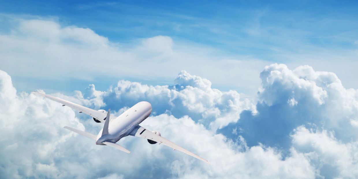A white airplane flying above fluffy clouds under a clear blue sky.