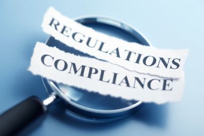 Magnifying glass highlighting compliance and regulations text.