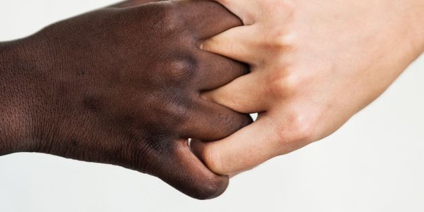 Two hands of different skin tones holding each other tightly.